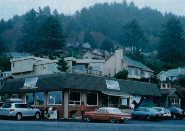This may contain: cars are parked in front of a small building on the side of a road with mountains in the background